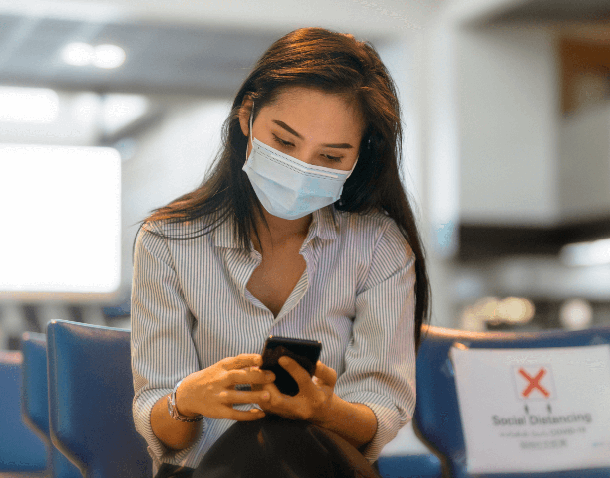 Mujer con mascarilla sentada en una silla utilizando su celular