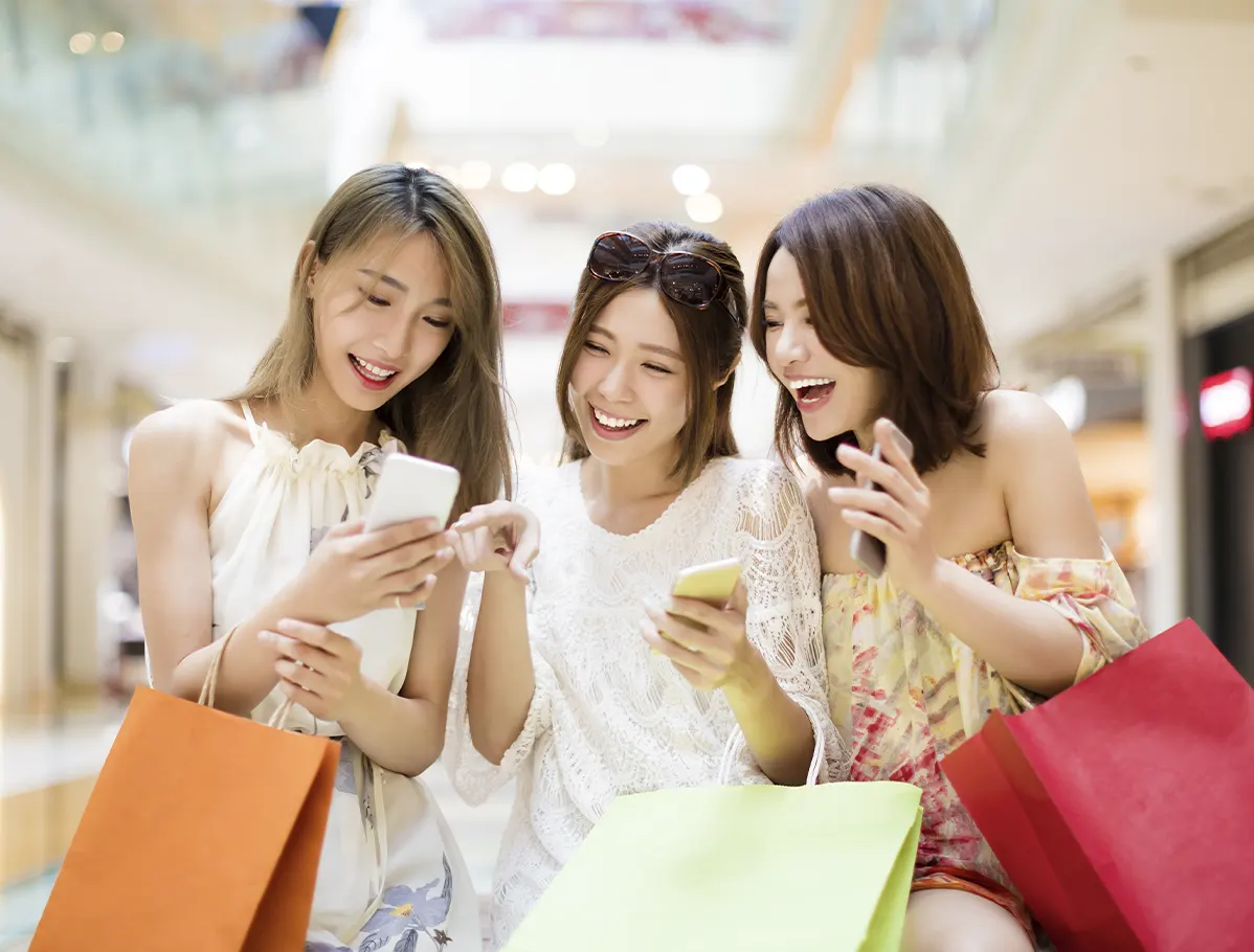 Tres mujeres riéndose con algunas compras en sus brazos revisando sus smartphones